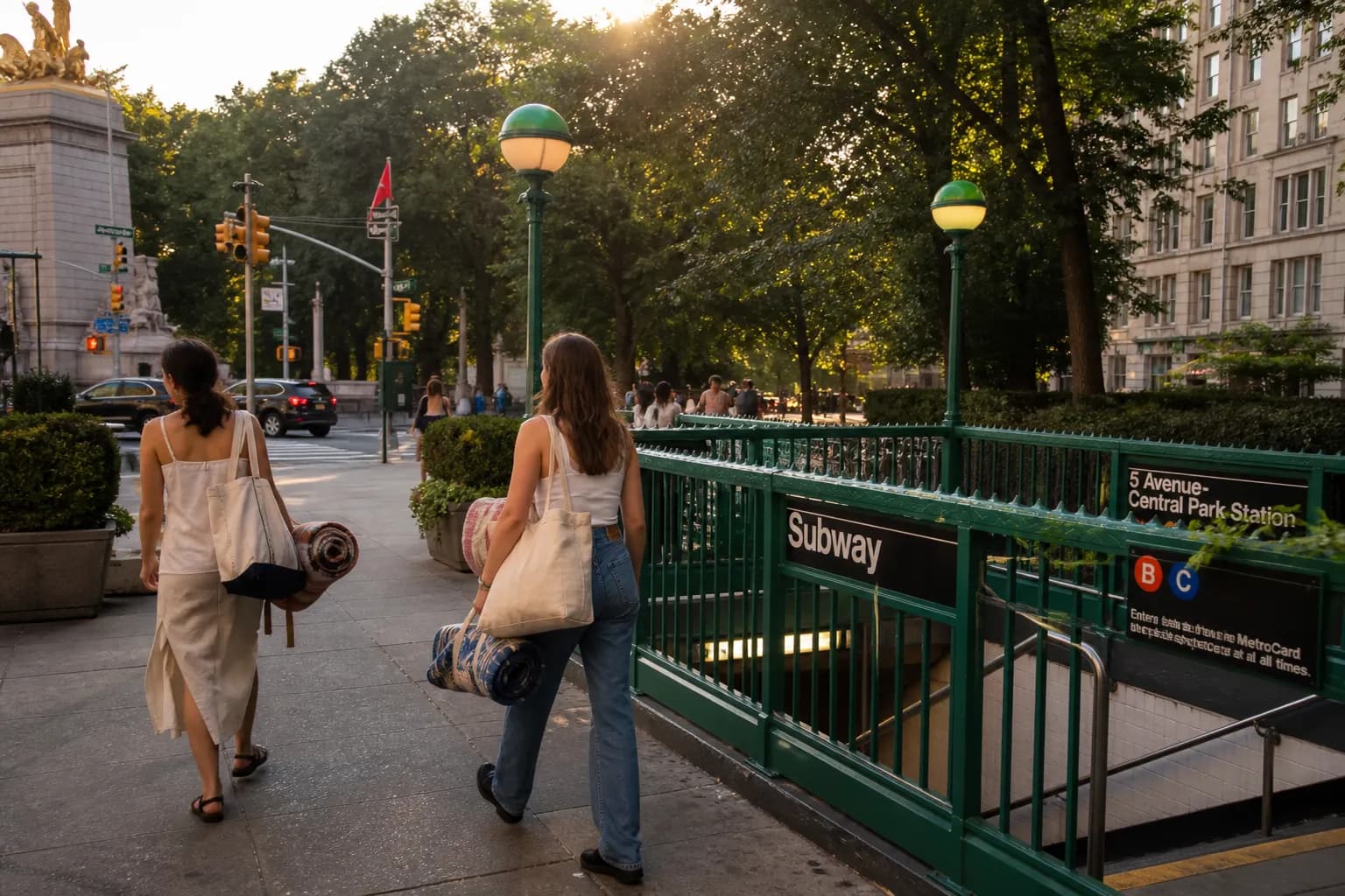 Young adults carrying picnic blankets walk past a classic green NYC subway entrance near Central Park at golden hour.