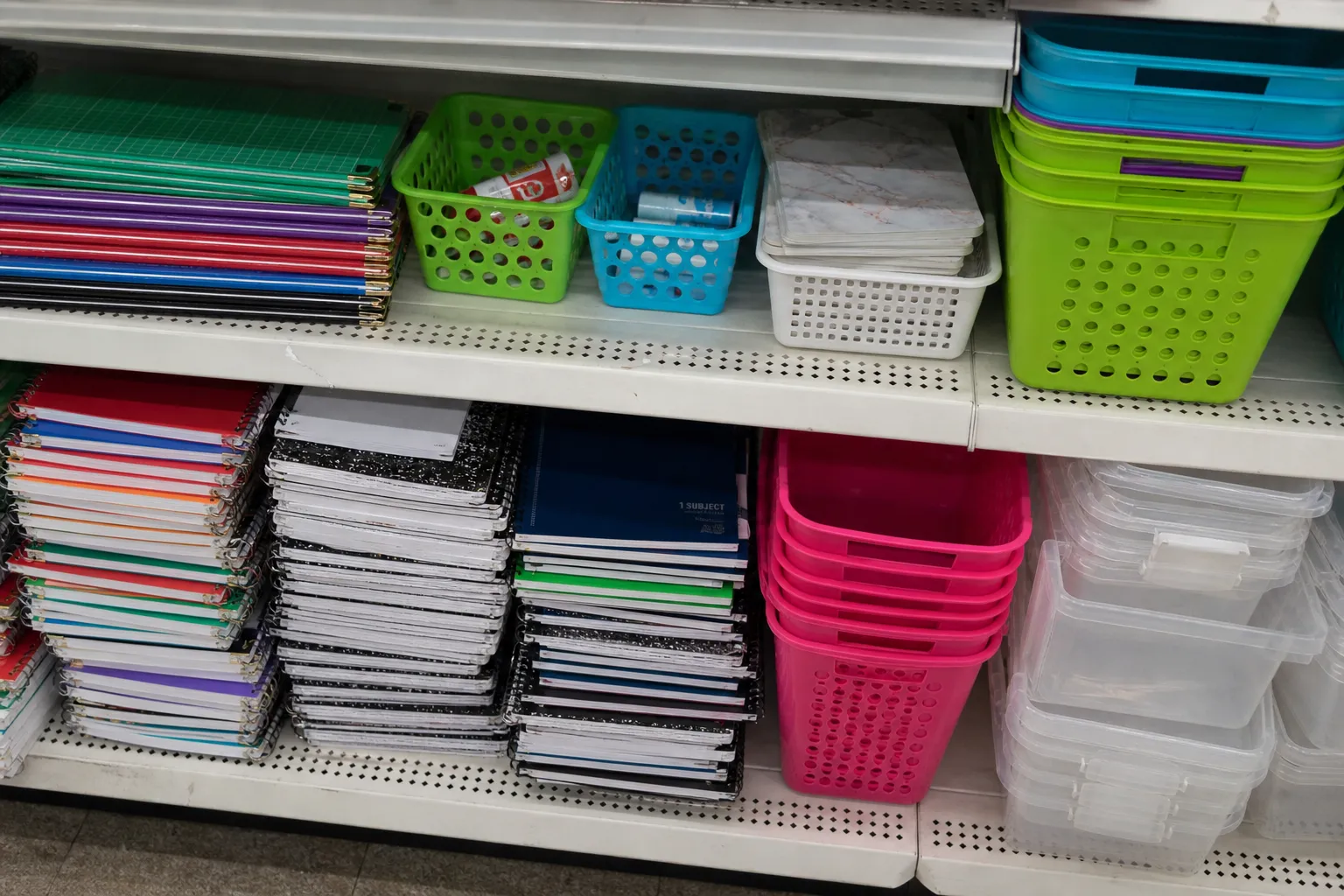 Close-up of organized plastic storage baskets and school supplies on store shelves.