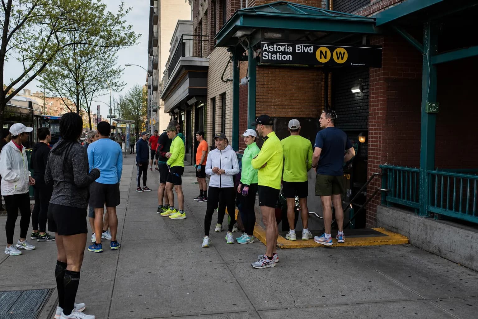 A busy Manhattan subway entrance on a sunny morning, with locals carrying gym bags and athletic gear as they walk past.