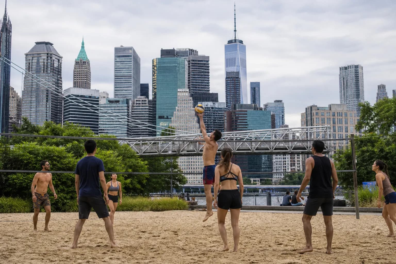 A volleyball match on the outdoor courts at Pier 2 in Brooklyn Bridge Park with the Manhattan skyline behind.
