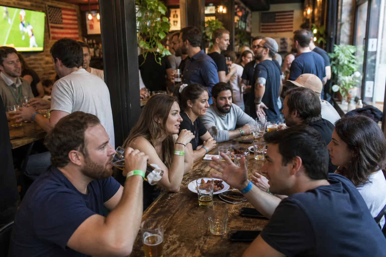 A group of young adults laughing and talking at a wooden table inside an Upper West Side sports pub.