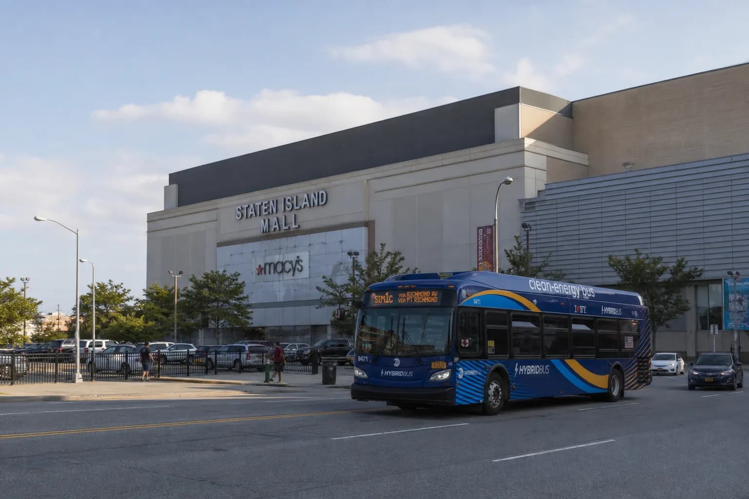 Wide-angle view of a transit bus driving past a suburban shopping center plaza near Staten Island.