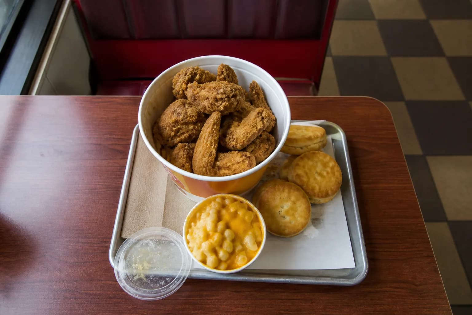 An overhead view of a KFC chicken bucket, biscuits, and mac and cheese on a tray inside a Queens restaurant.