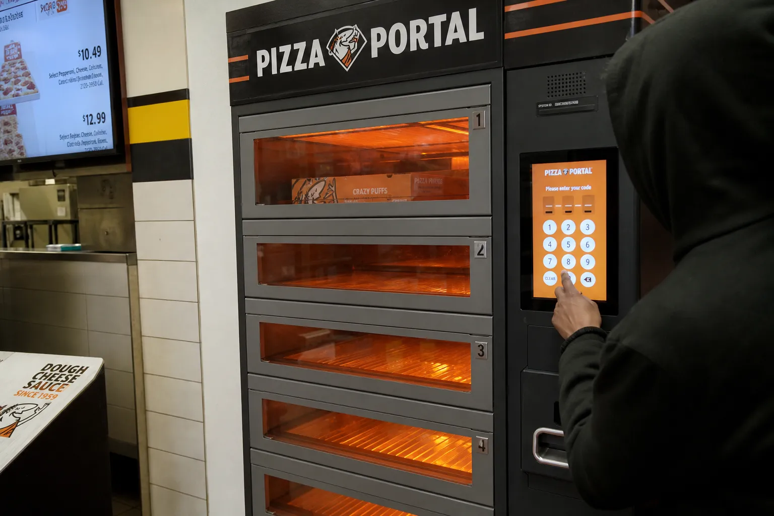 A view of the interior counter of a Bronx Little Caesars location with a Pizza Portal pickup station and workers prepping fresh pizzas.