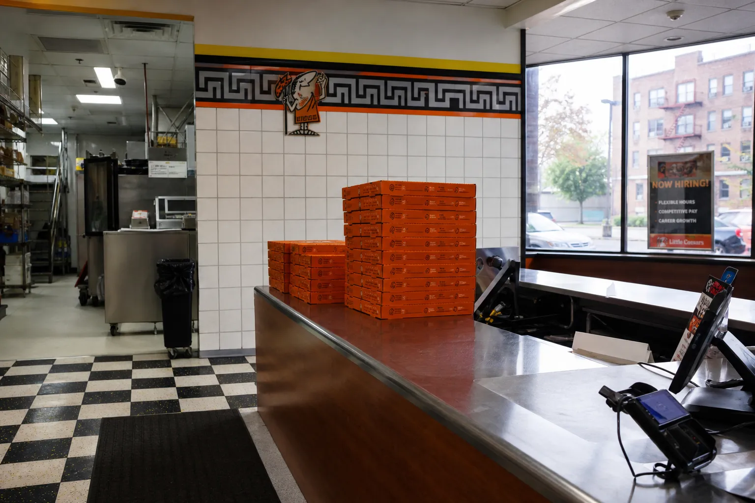 The clean metal counter and stacked pizza boxes inside the quiet Morris Park Little Caesars location.
