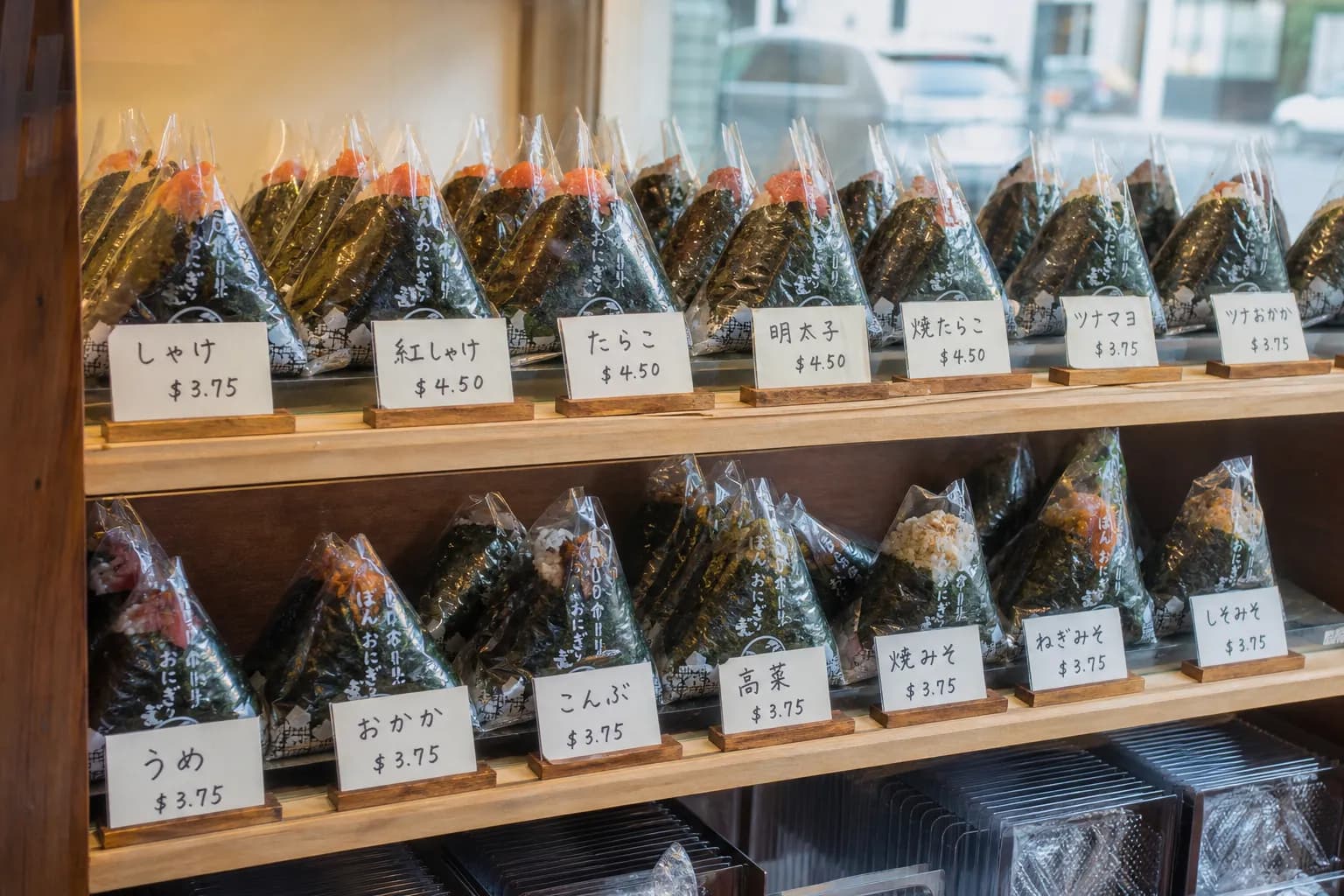 Triangular Japanese onigiri wrapped in plastic on a wooden shelf in an NYC grocery store.