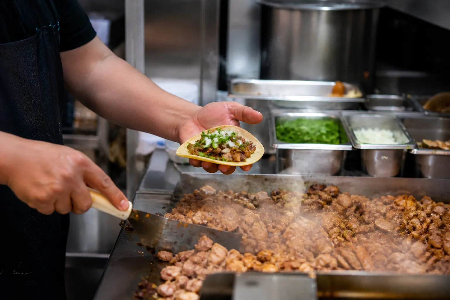 Chef assembling a pork taco with cilantro and onion at a busy Midtown counter.