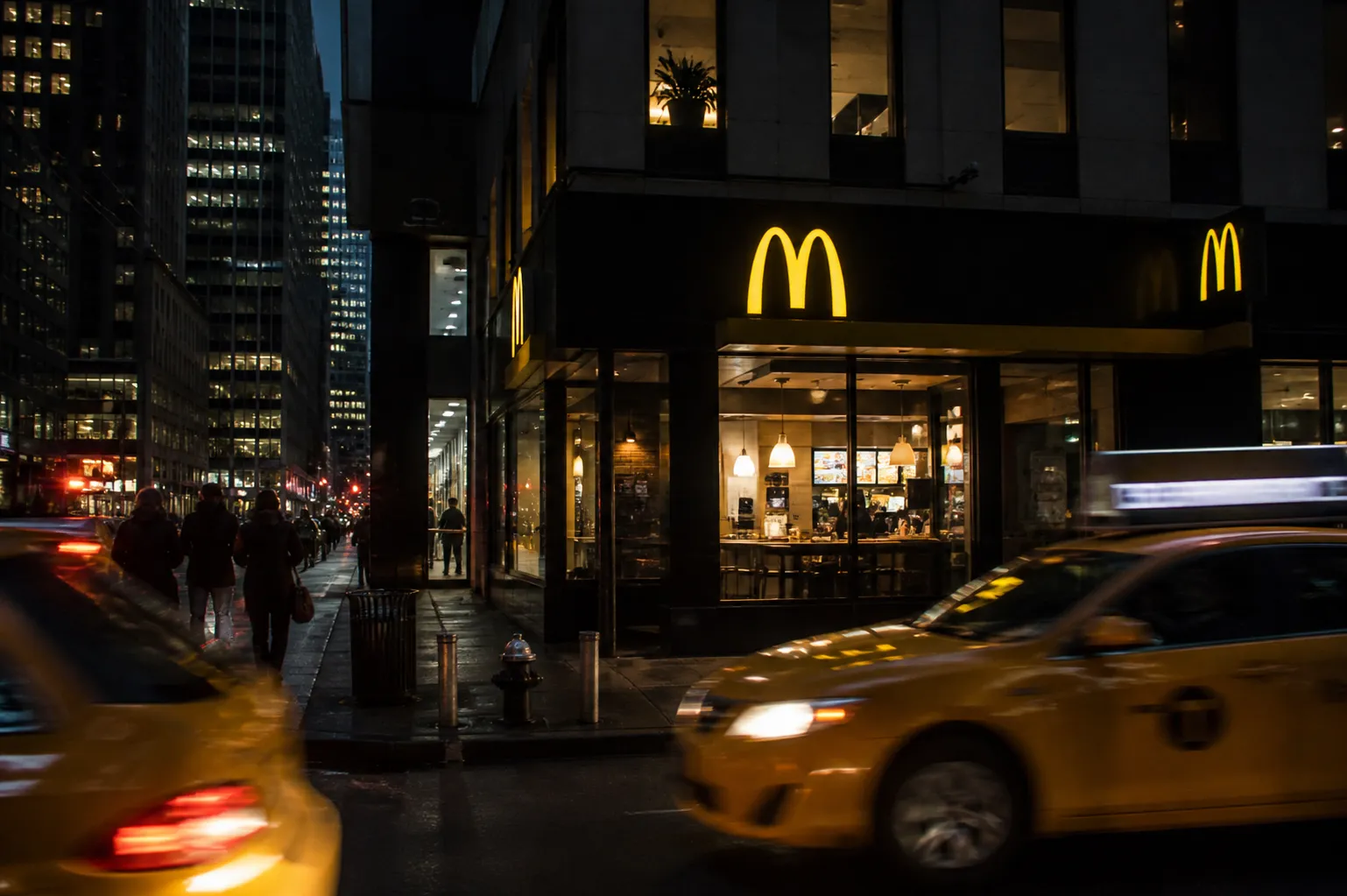 A glowing McDonald's golden arches sign on a wet Manhattan street corner at dawn, reflecting city lights.