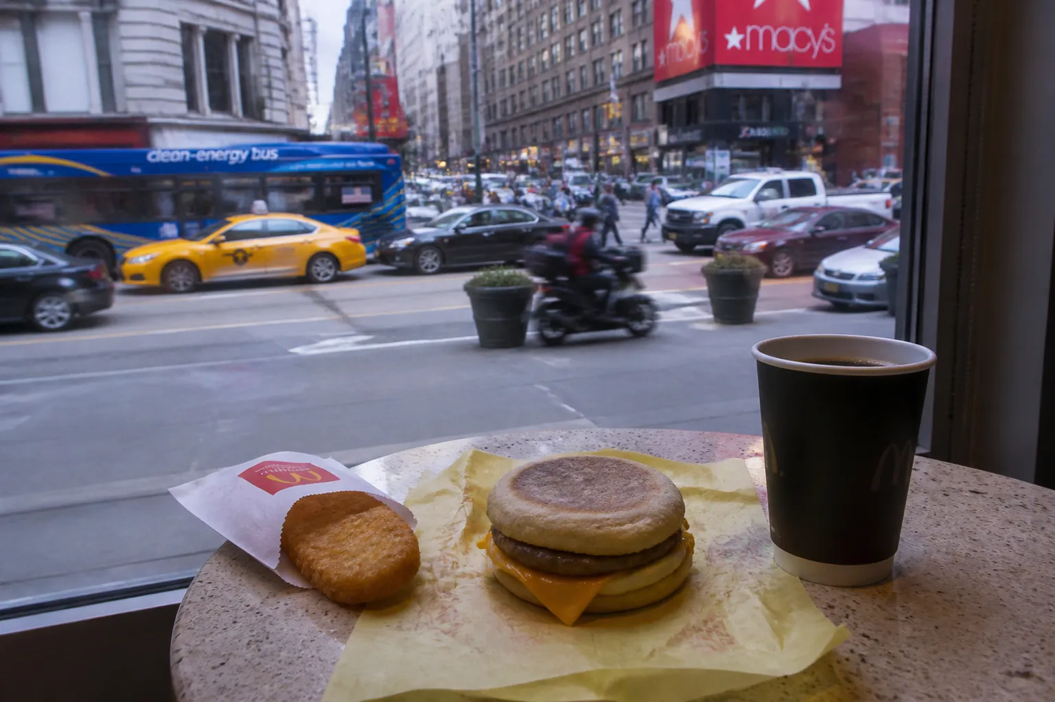 A classic McDonald's breakfast combo of McMuffin, hash brown, and coffee near a window overlooking Herald Square.