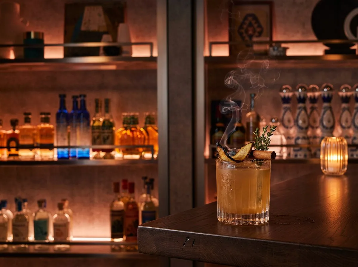 Close-up of a mezcal cocktail and agave spirit bottles lit in warm red bar light
