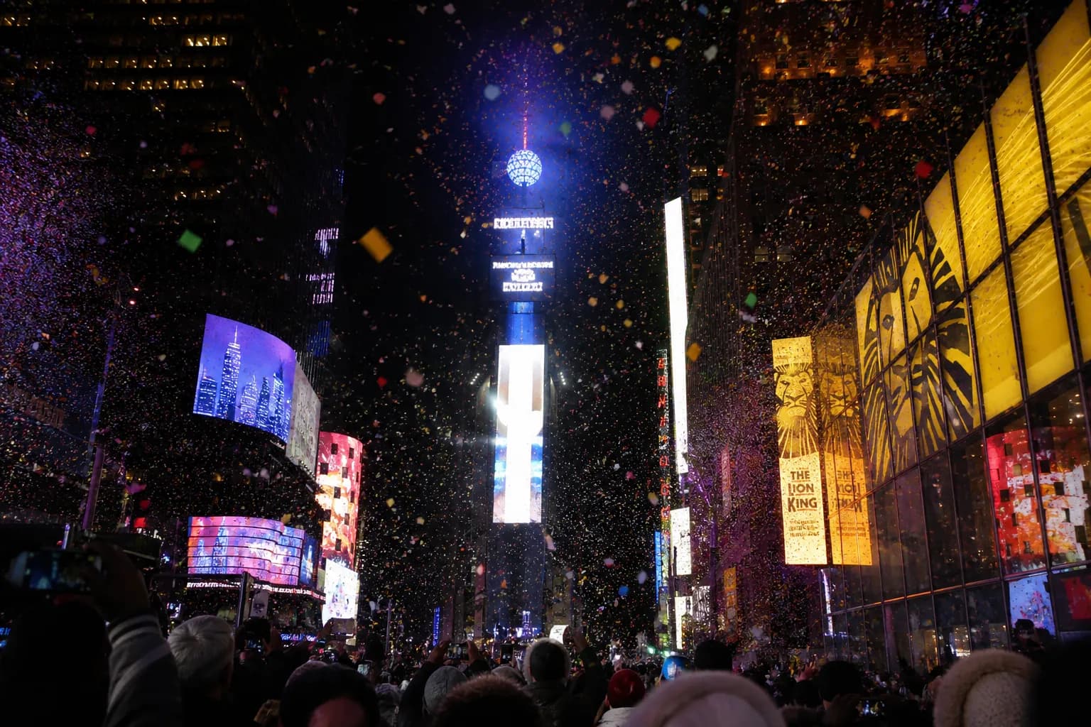 The bright New Year's Eve ball drop surrounded by colorful billboards and falling confetti in Times Square.