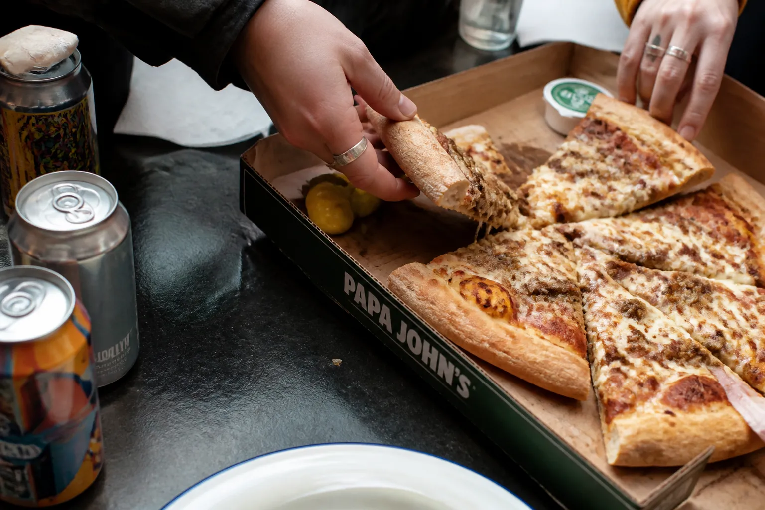 Close-up of hands grabbing pizza slices next to Brooklyn craft beer cans.