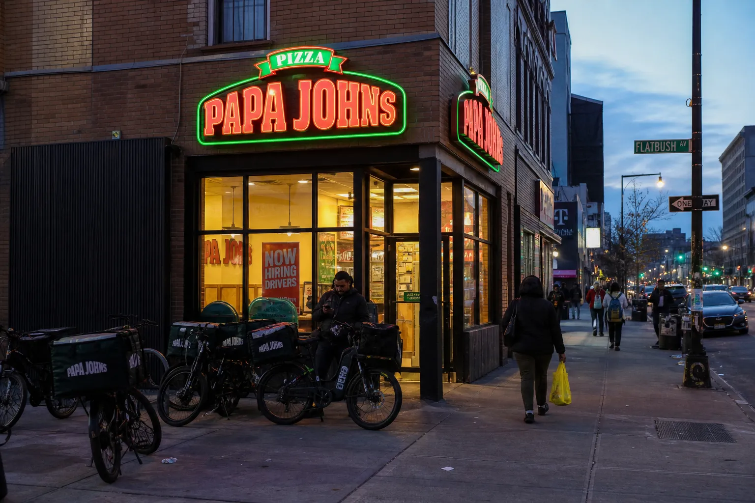 The neon storefront of the Flatbush Avenue Papa Johns in Brooklyn at dusk.