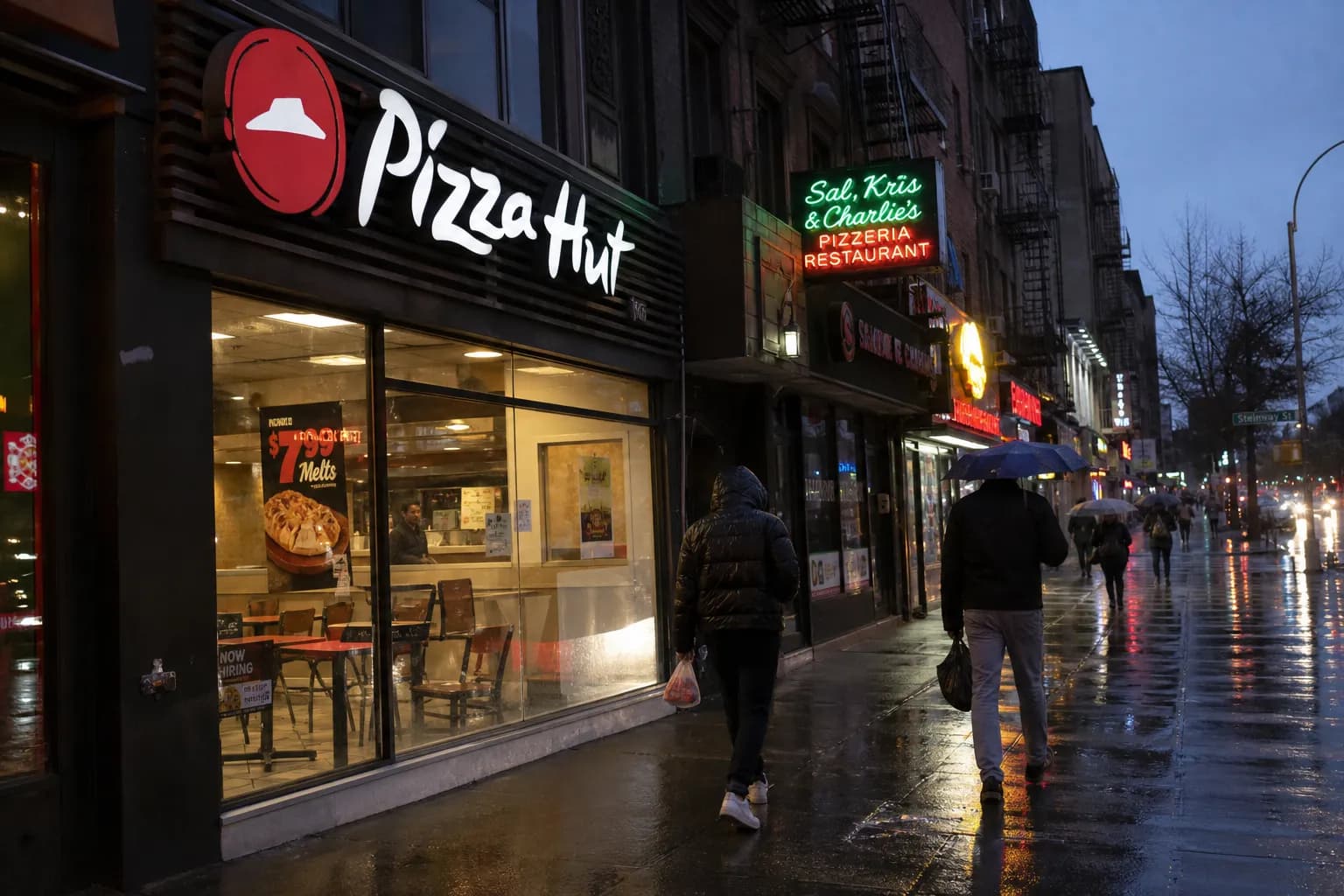 Pedestrians walking past storefronts and a Pizza Hut on Steinway Street in Astoria, Queens.