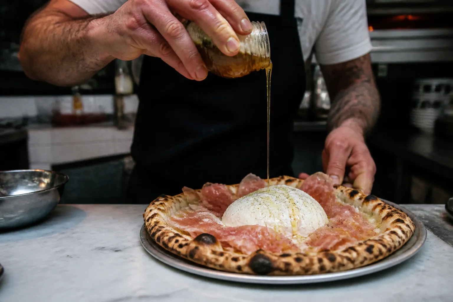 A fresh, crispy slice of pizza topped with burrata and hot honey being prepared on a counter.