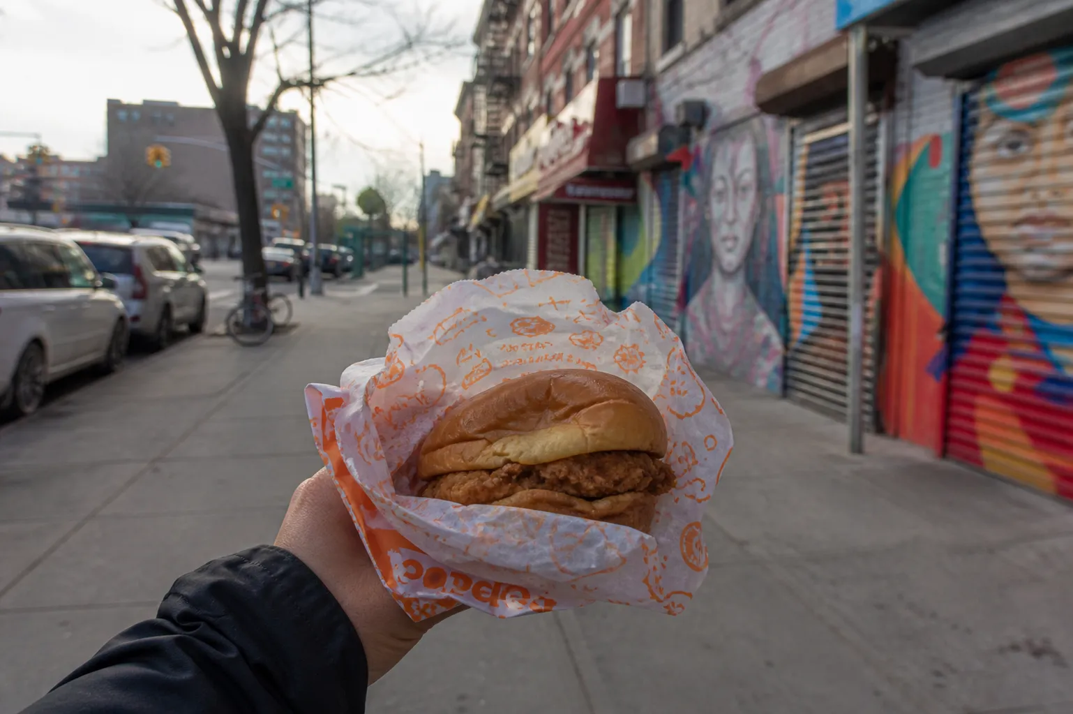 A Popeyes chicken sandwich held up against the backdrop of an East Harlem street scene.