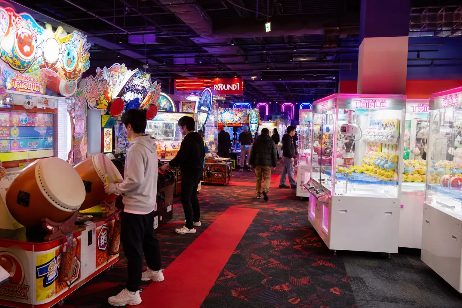 A wide-angle shot of the glowing neon games and bowling lanes inside the Round 1 arcade at The Shops at Skyview in Flushing, Queens.