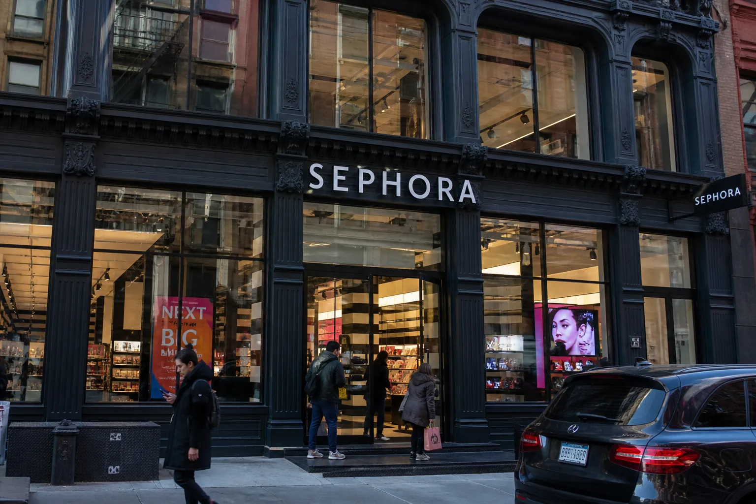 The illuminated modern glass facade of a large cosmetics store on a busy Manhattan street.