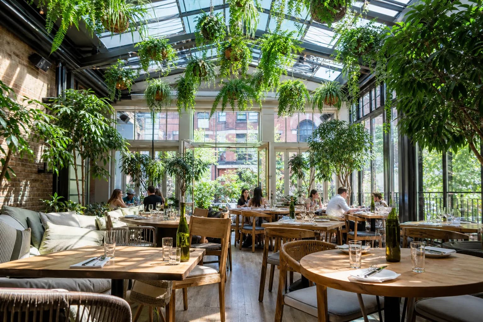 Wide view of the bright, plant-filled glass conservatory dining room at Sixty Vines in NYC with guests enjoying brunch.