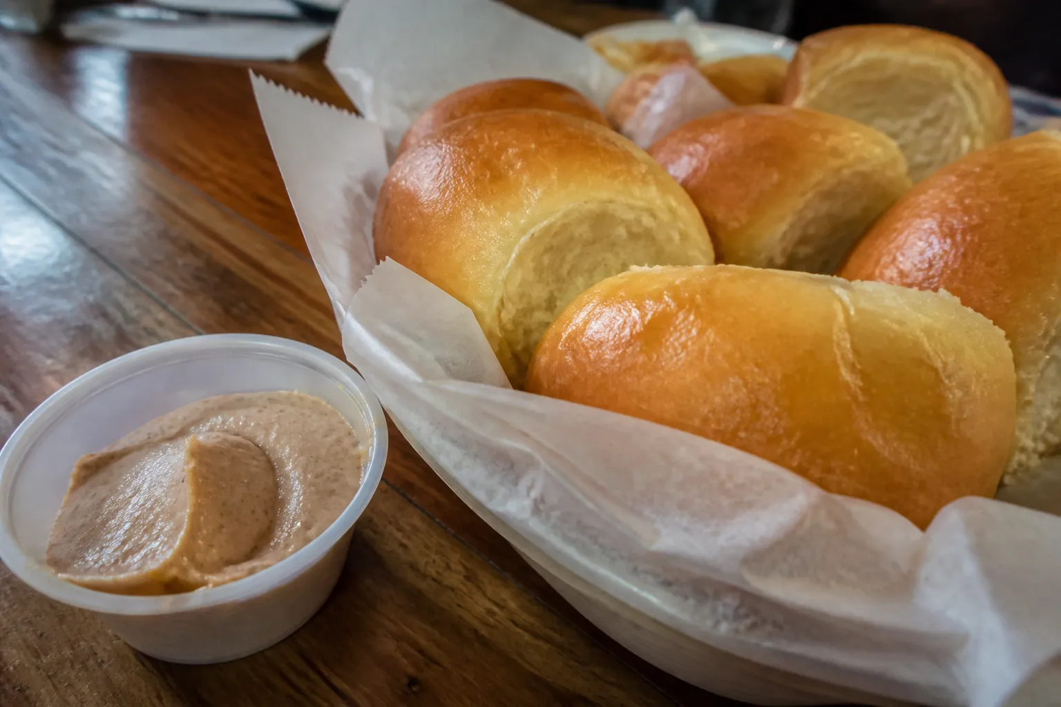 A basket of fresh, warm yeast rolls served with cinnamon honey butter on a rustic table.