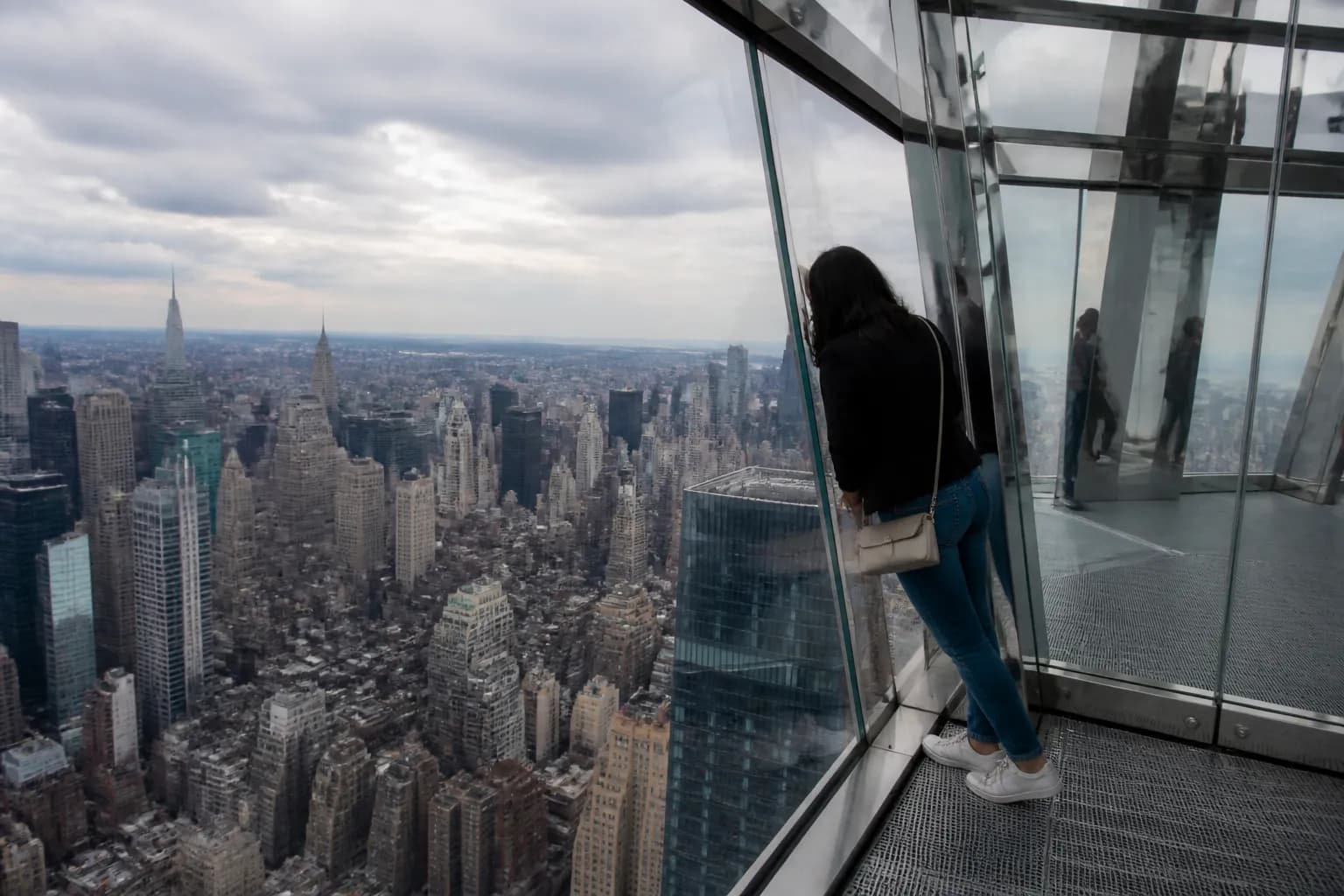 A visitor standing at the narrow tip of the glass deck of The Edge NYC, leaning over the city below.