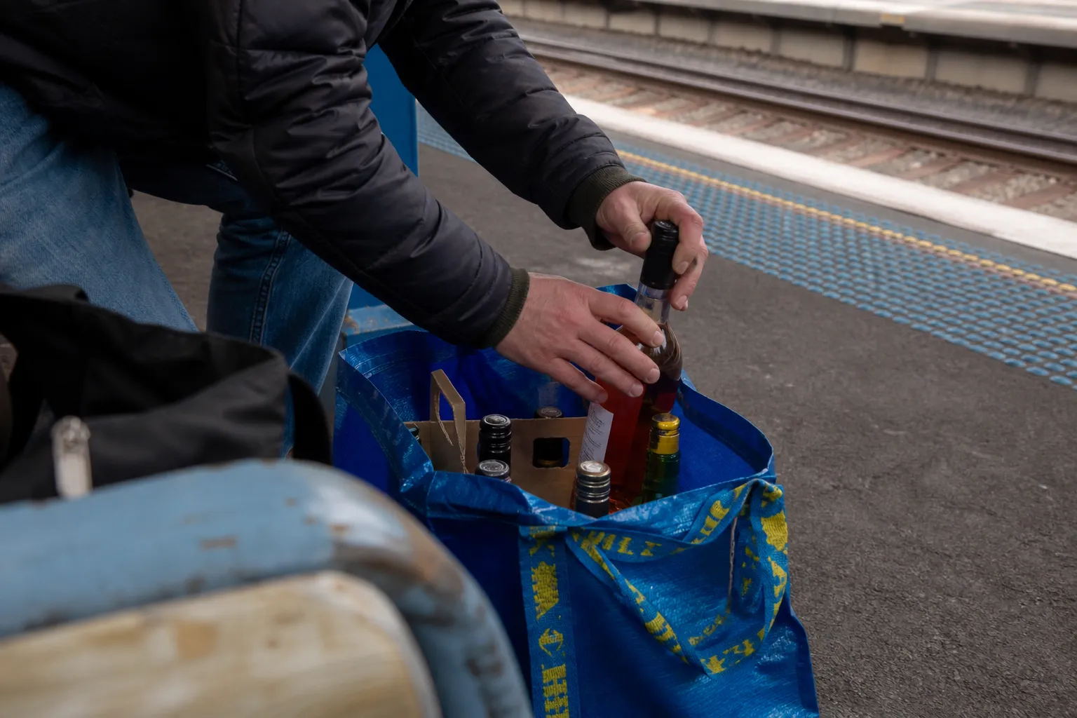 Close-up of glass bottles being organized into a sturdy blue shopping bag on a transit platform.