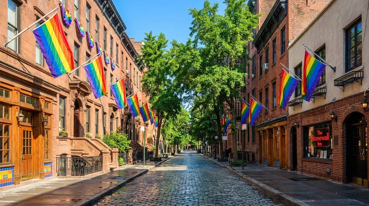 Bright sunny day West Village street view of historic Christopher Street with rainbow flags hanging from brownstone facades, leafy summer canopy, polished cobblestone street, vivid blue sky, colorful 