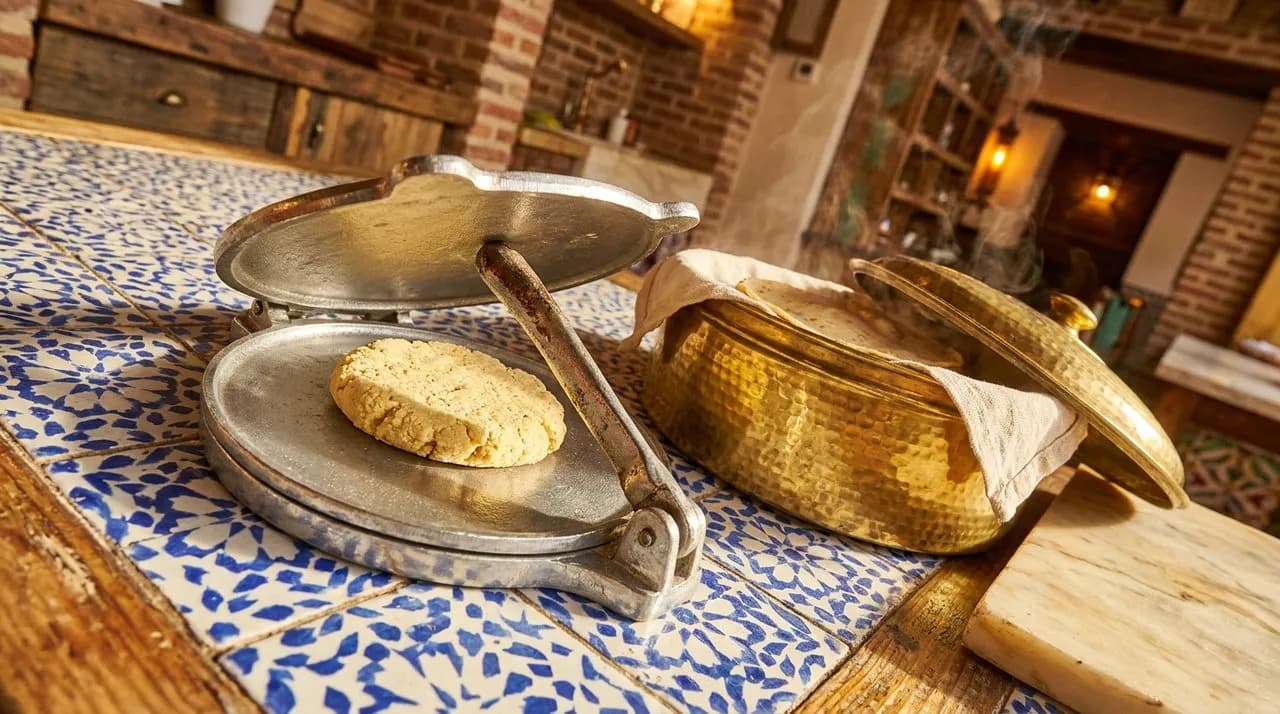 Extreme close-up of Bushwick Mexican counter tortilla press, polished metal press, masa texture, brass tortilla warmer, patterned tile surface, warm light