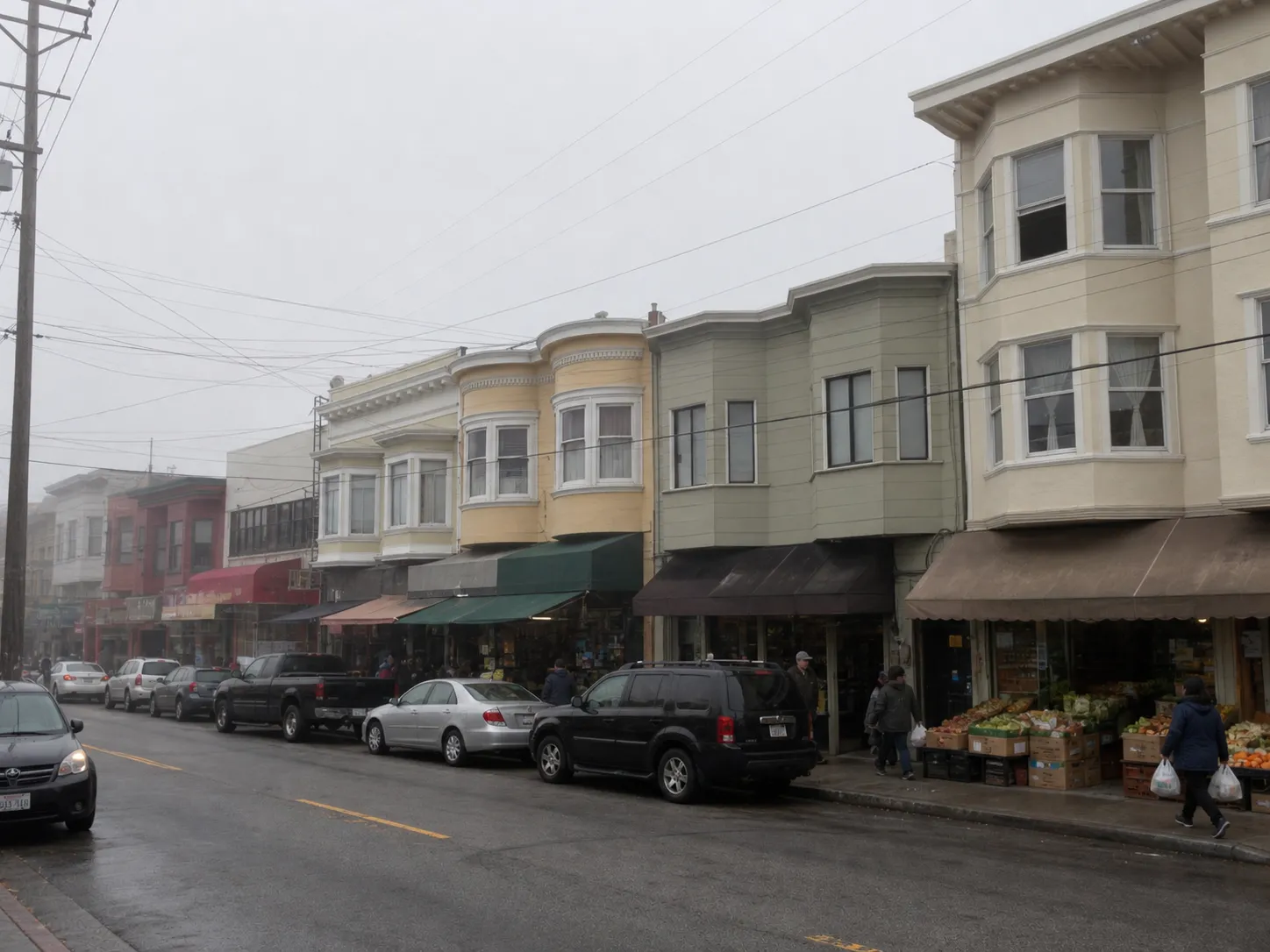 Eye-level view down a foggy Inner Richmond commercial street in San Francisco with two-storey bay-window buildings, cloth awnings, produce crates on the sidewalk and shoppers carrying bags