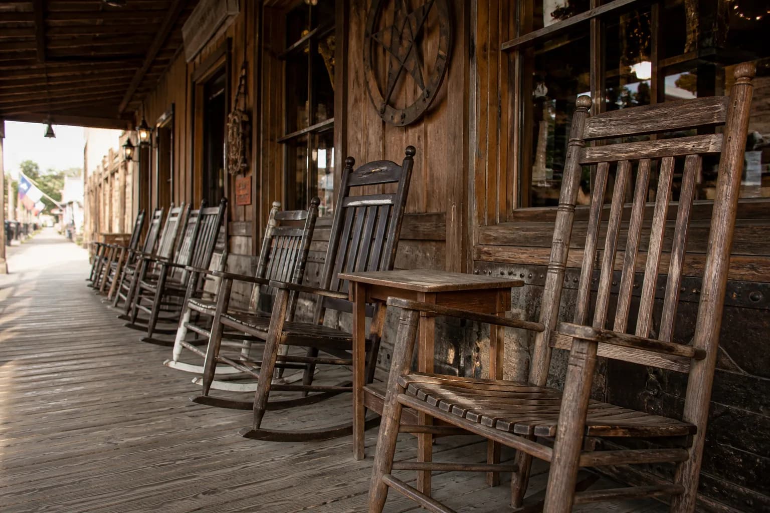 Wooden rocking chairs lined up on a rustic country porch under warm sunlight.