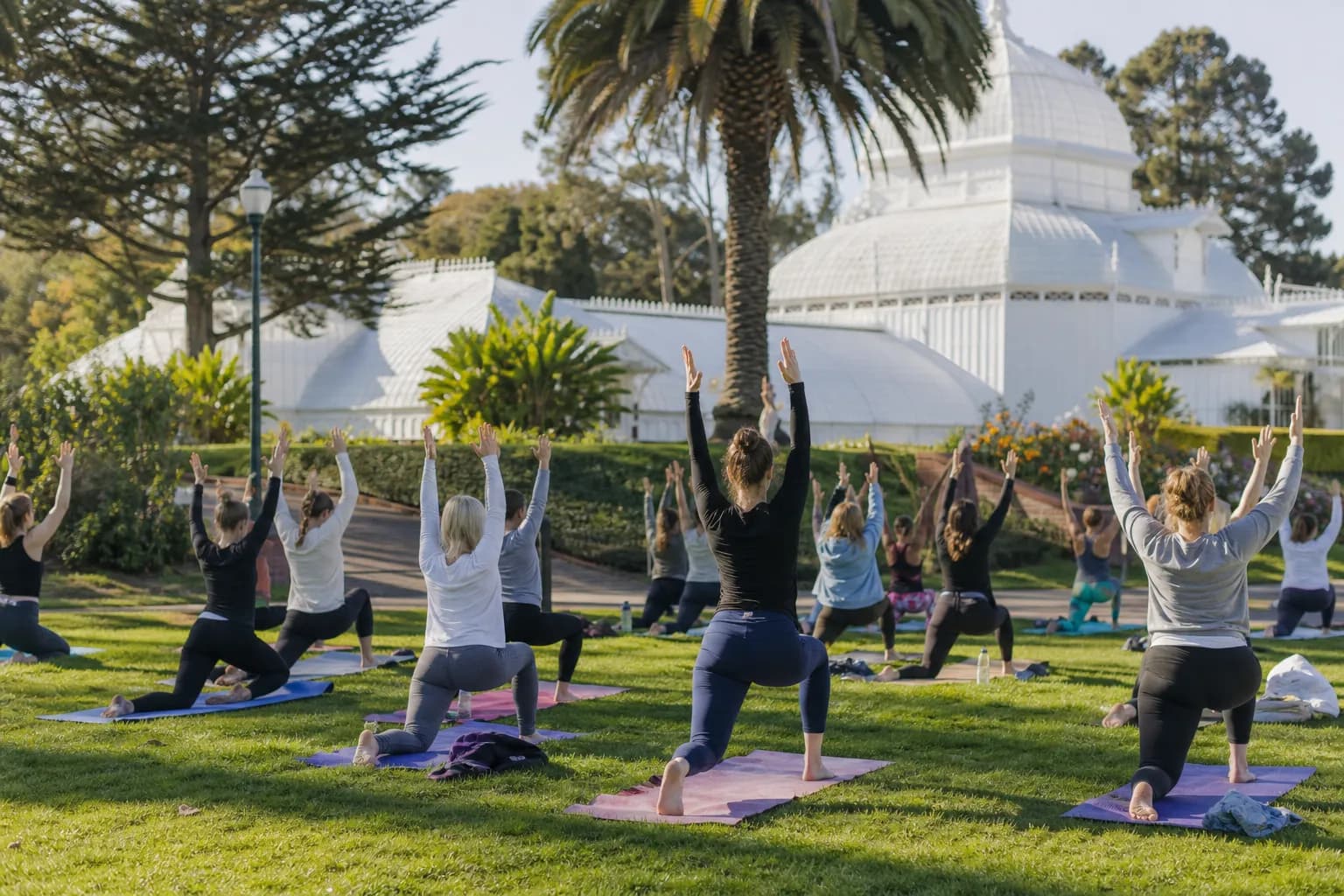 Outdoor community yoga session on a green lawn in front of the Conservatory of Flowers in Golden Gate Park.