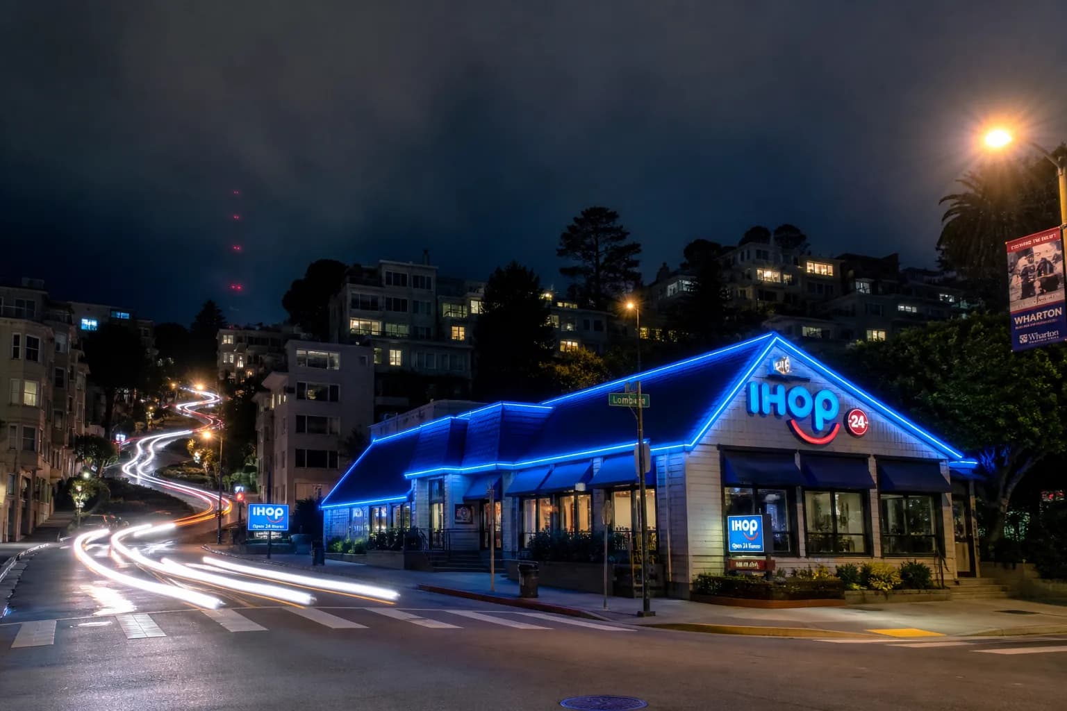 A glowing neon blue roof sign of an IHOP restaurant reflecting off damp San Francisco pavement at night.