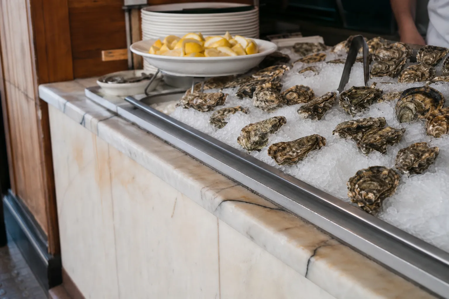 The bustling interior counter of a classic San Francisco seafood restaurant, featuring fresh oysters on ice and patrons dining on wooden stools.