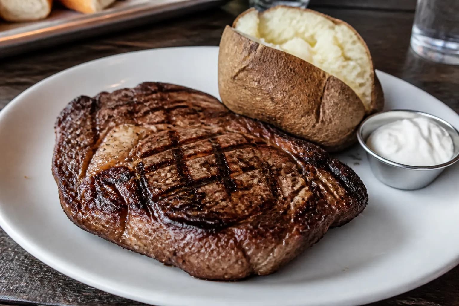 A juicy, hot ribeye steak fresh off the grill with a loaded baked potato on a rustic dining table.