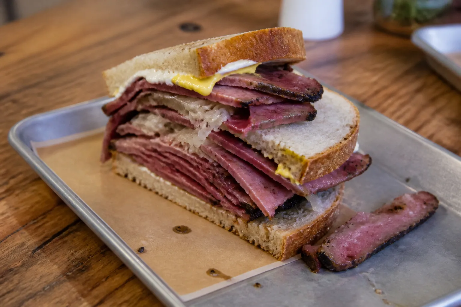 A thick, freshly sliced pastrami and cheese sandwich on rye bread sitting on a metal deli tray.