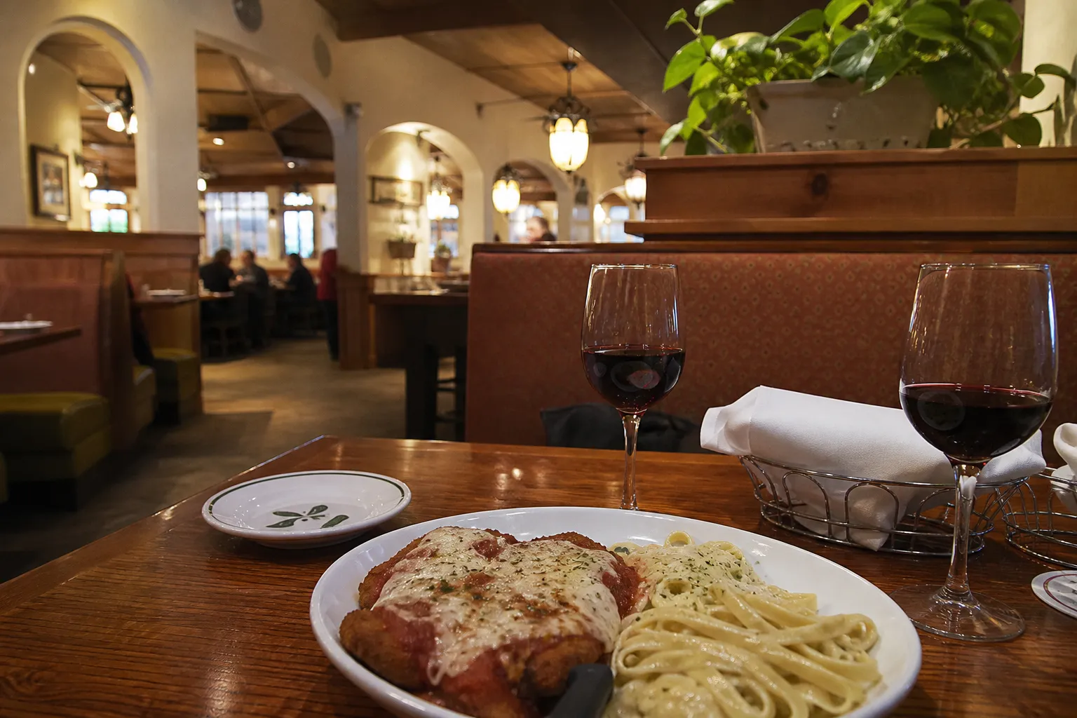 A classic date night meal of chicken parmigiana and red wine in a cozy restaurant booth.