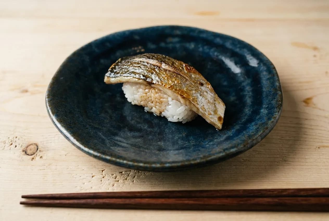 Spanish mackerel nigiri with crispy skin on dark ceramic plate with hinoki wood surface