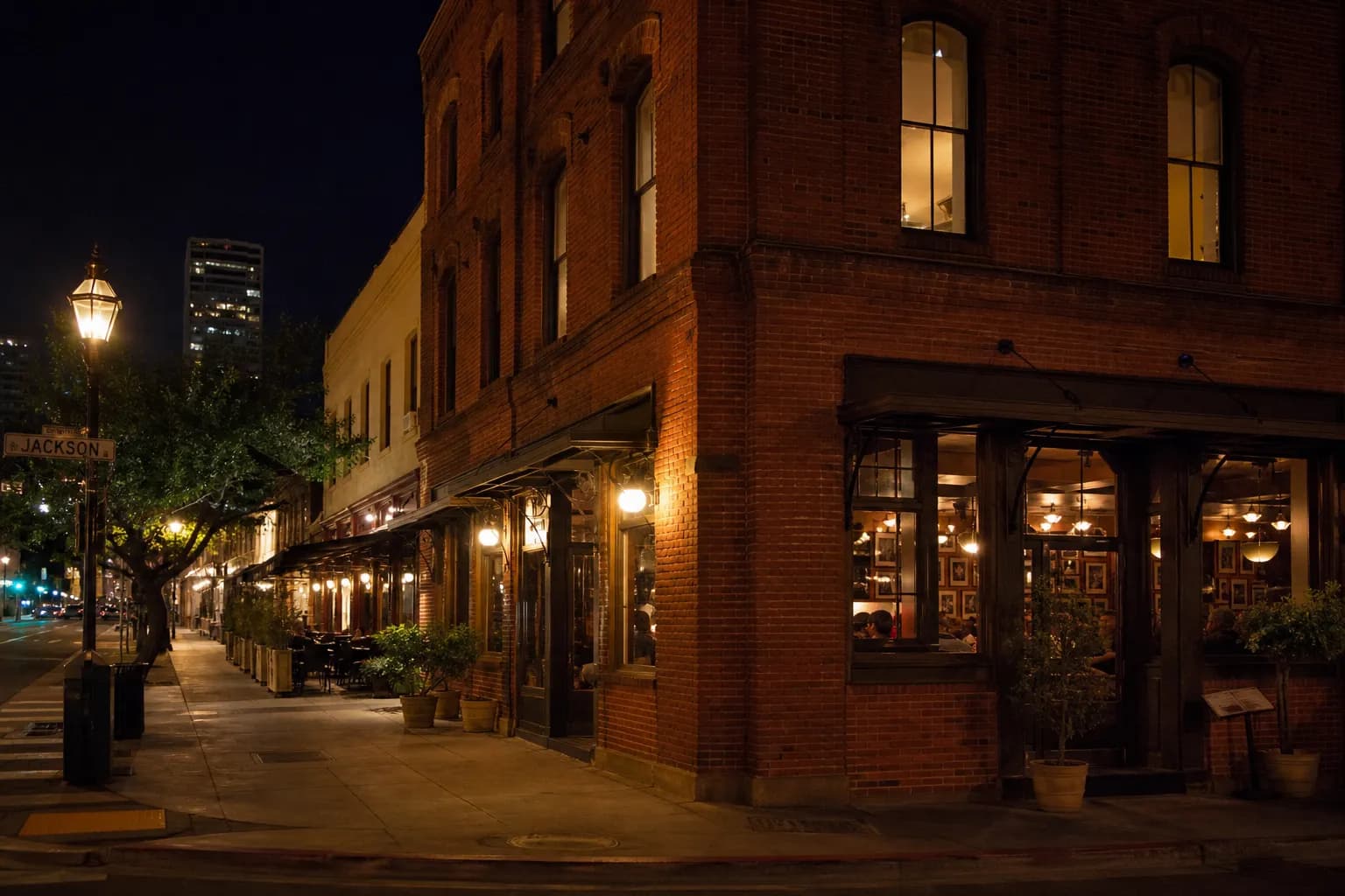 A warm, glowing exterior of a San Francisco restaurant at night, with patrons visible through large windows under streetlights