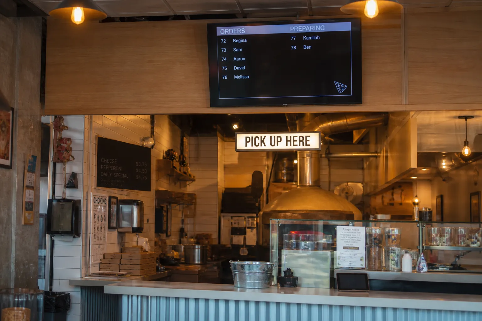 The bright interior of a pizza pickup counter with warm lights and an order pickup station.