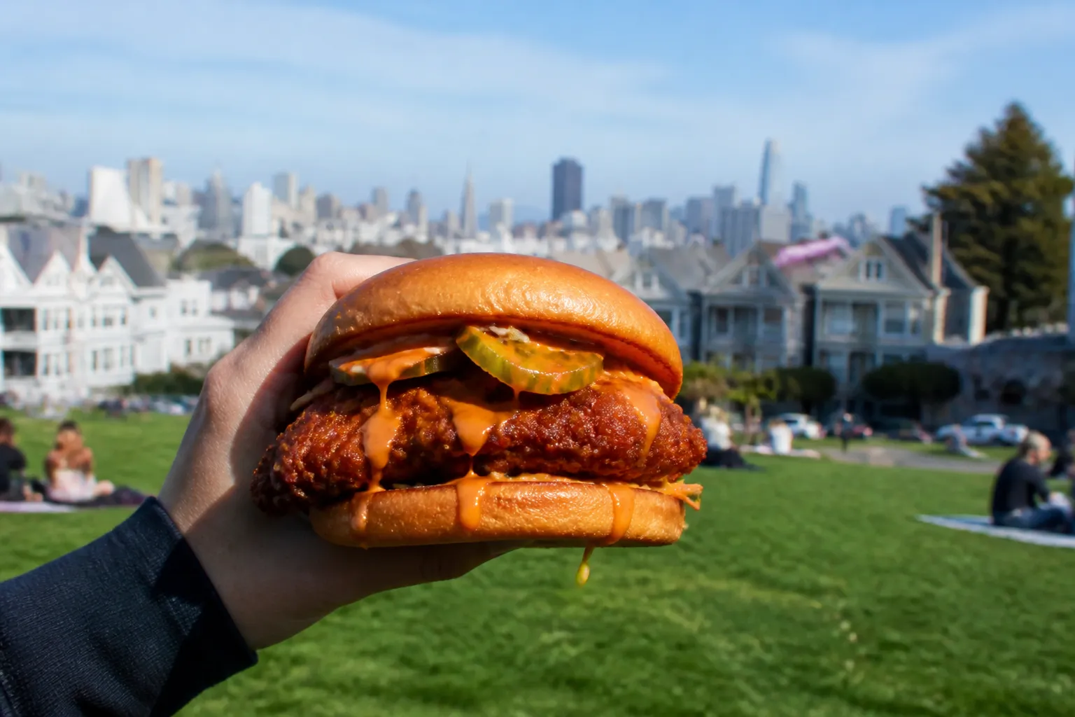 A thick fried chicken sandwich with pickles and sauce held outdoors in SF