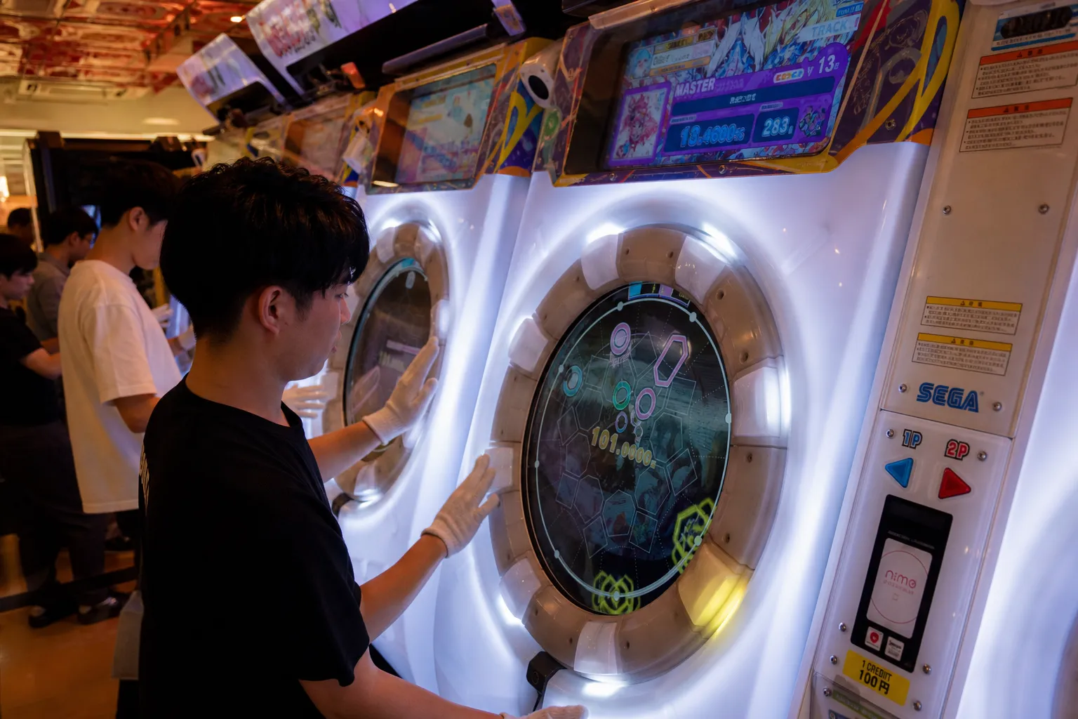 Close-up of Japanese rhythm arcade games with glowing buttons and players wearing gloves.