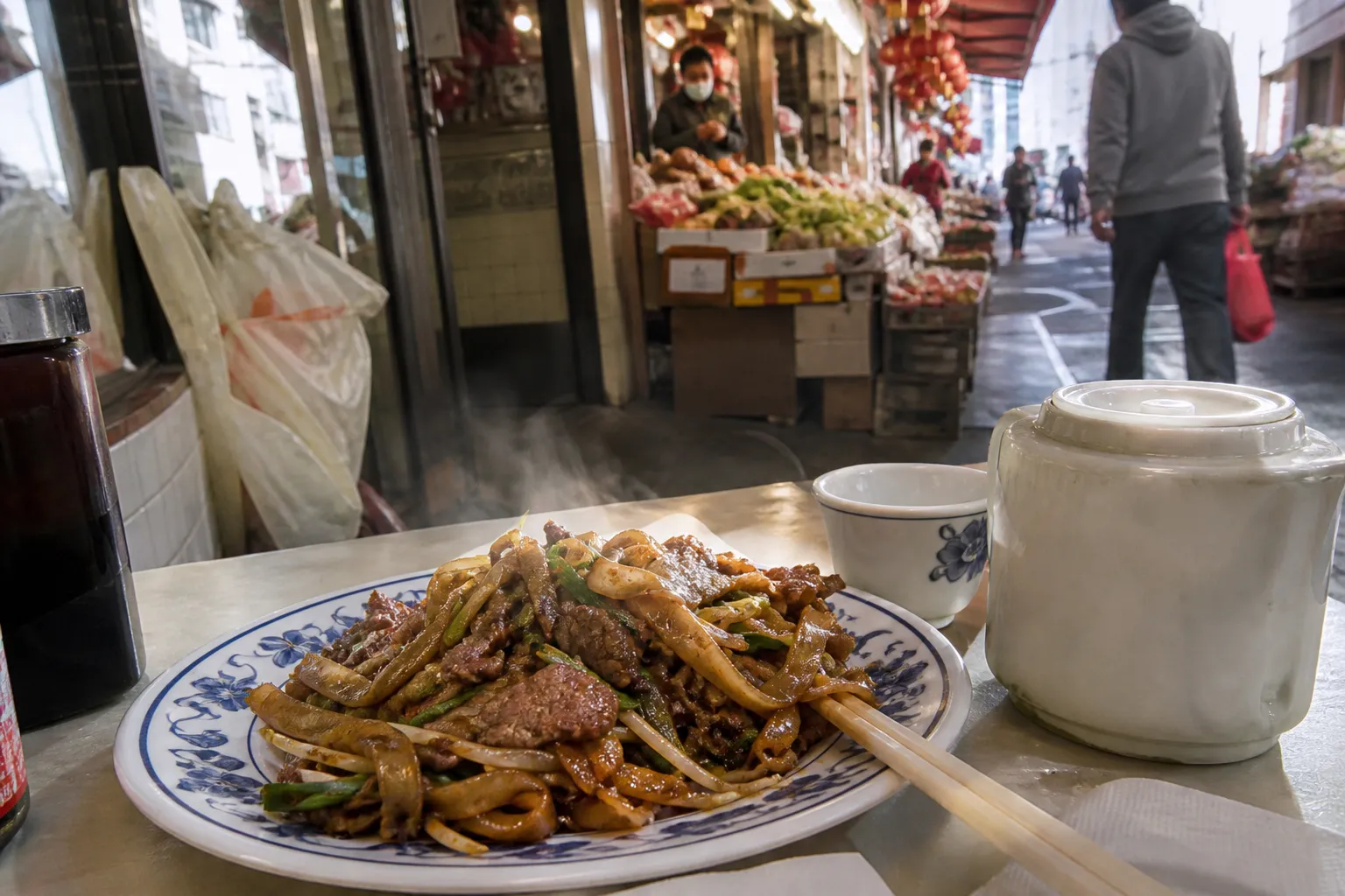 Steaming plates of stir-fried noodles and rice dishes in a busy San Francisco Chinatown market aisle