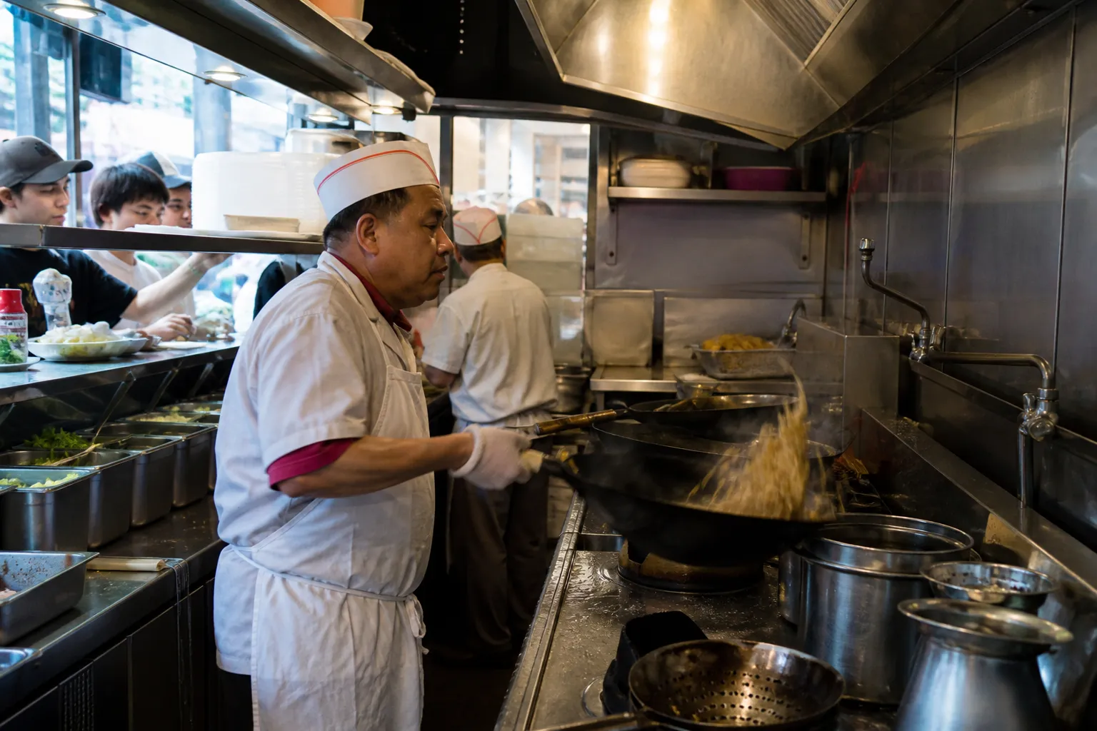 A cook tossing noodles at a hot wok station inside a Chinatown restaurant on Grant Avenue