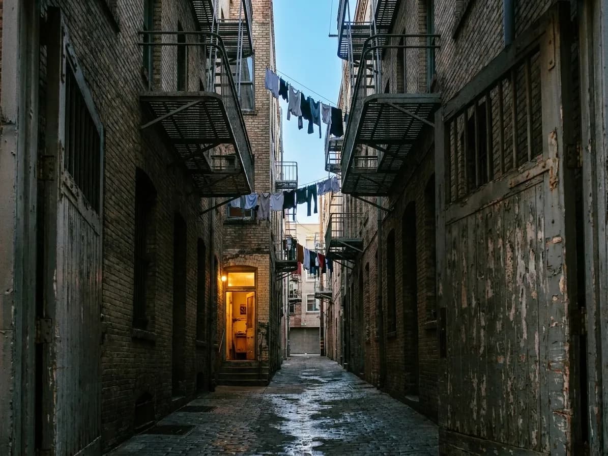 A narrow San Francisco alley between brick buildings with fire escapes above and a single lit doorway halfway down