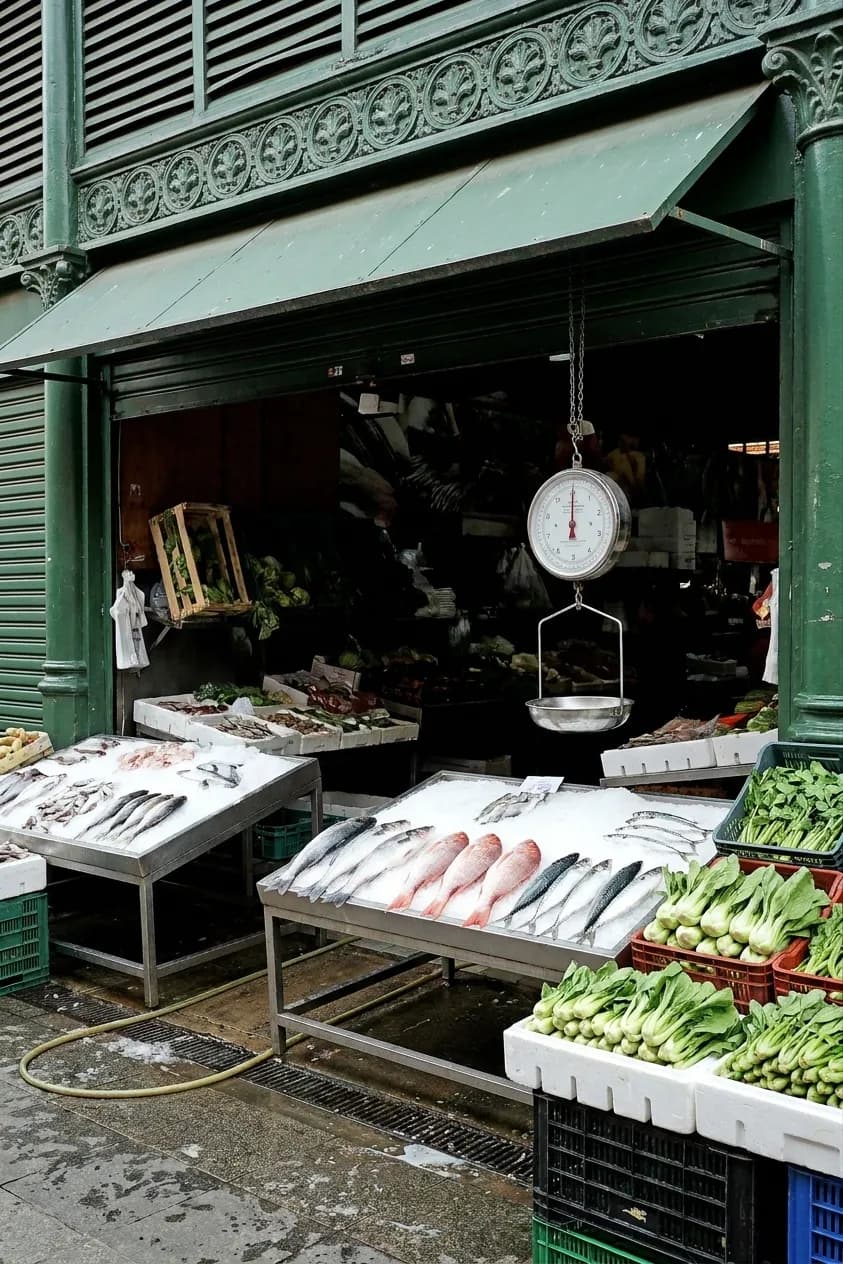 A Chinatown fish shop frontage with whole fish laid on tilted ice beds, crates of greens beside them and a hanging scale above