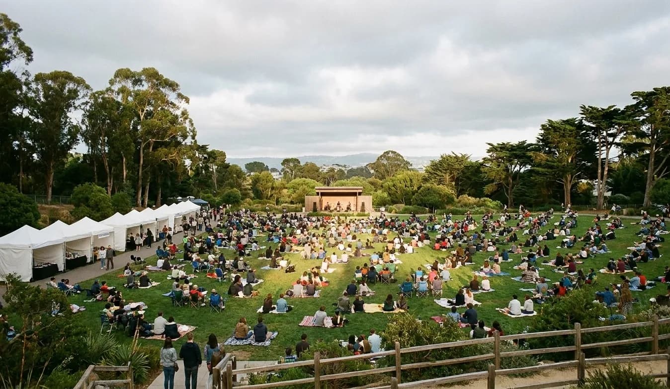 A free outdoor event on a sloping lawn in a large San Francisco park with several hundred people facing a small stage