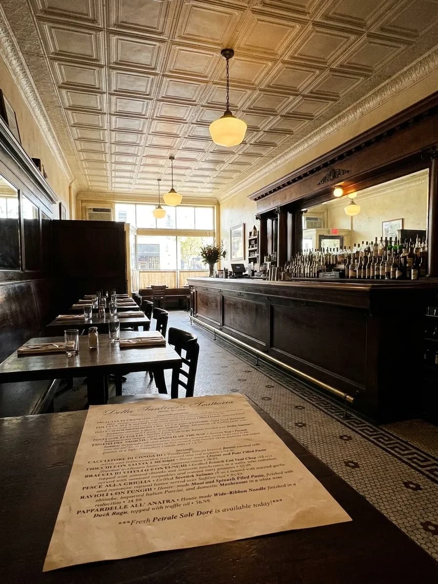 The interior of an old San Francisco bar with dark wooden booths, a tiled floor, a long mirror behind the back bar and a pressed-tin ceiling