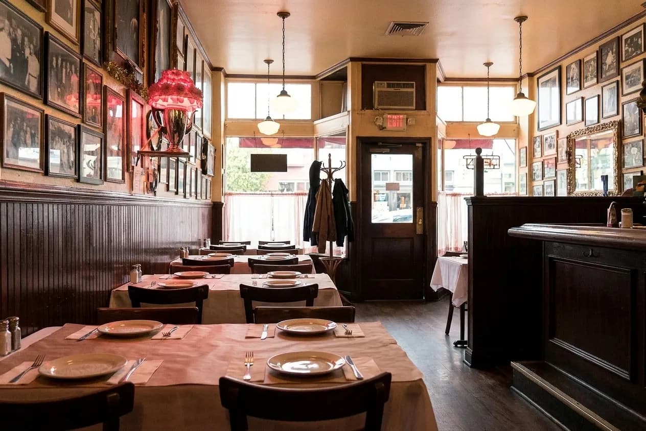 An old Italian-American dining room with white-clothed tables, dark panelling and framed photographs crowding the wall above