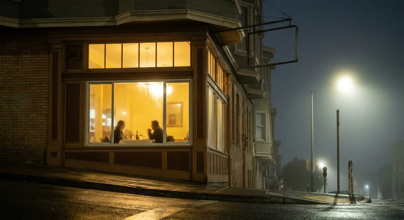 A San Francisco corner restaurant glowing warm on a foggy night, silhouettes inside and a wet sloping sidewalk catching the light