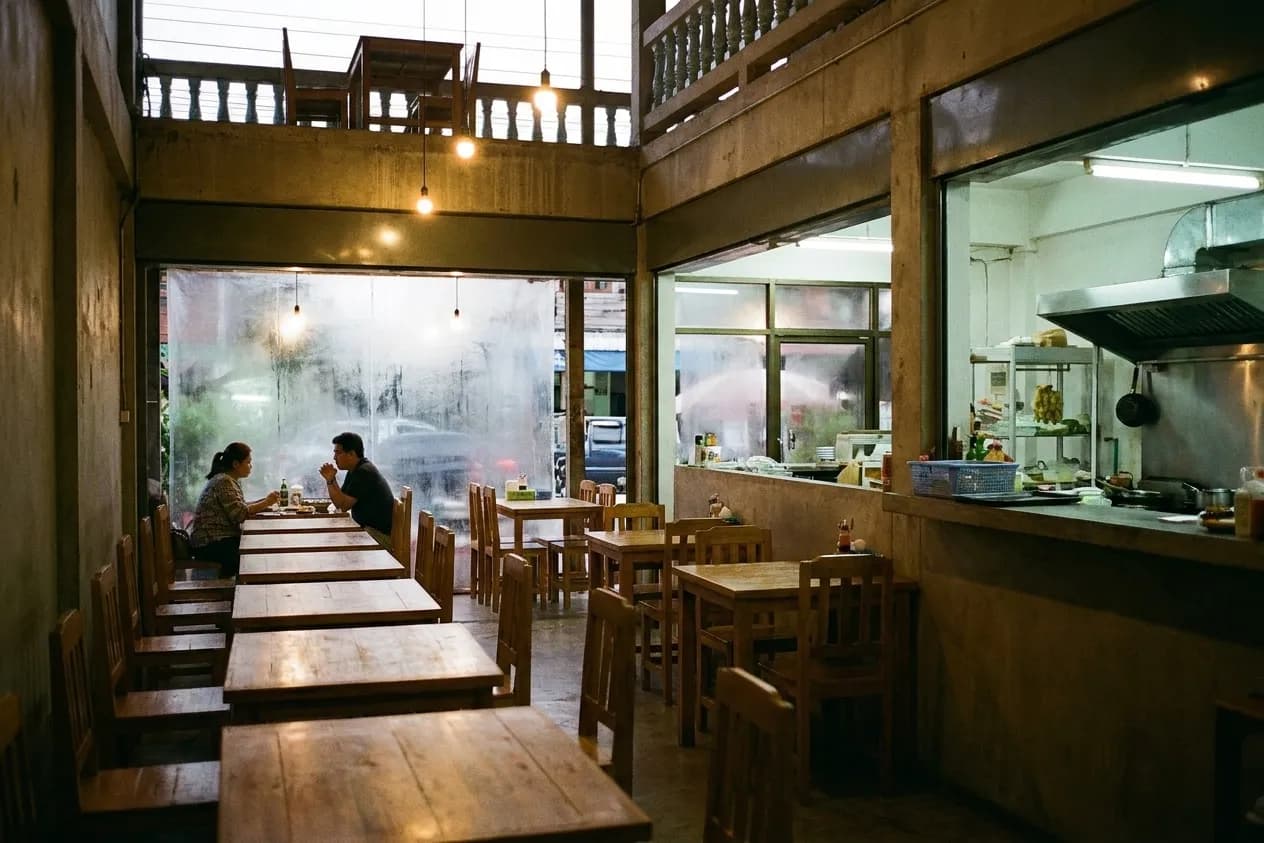 A small San Francisco neighbourhood restaurant with closely spaced wooden tables, a couple by the window and a bright kitchen pass at the back
